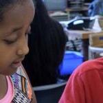 Two students work together at a desk in a classroom.