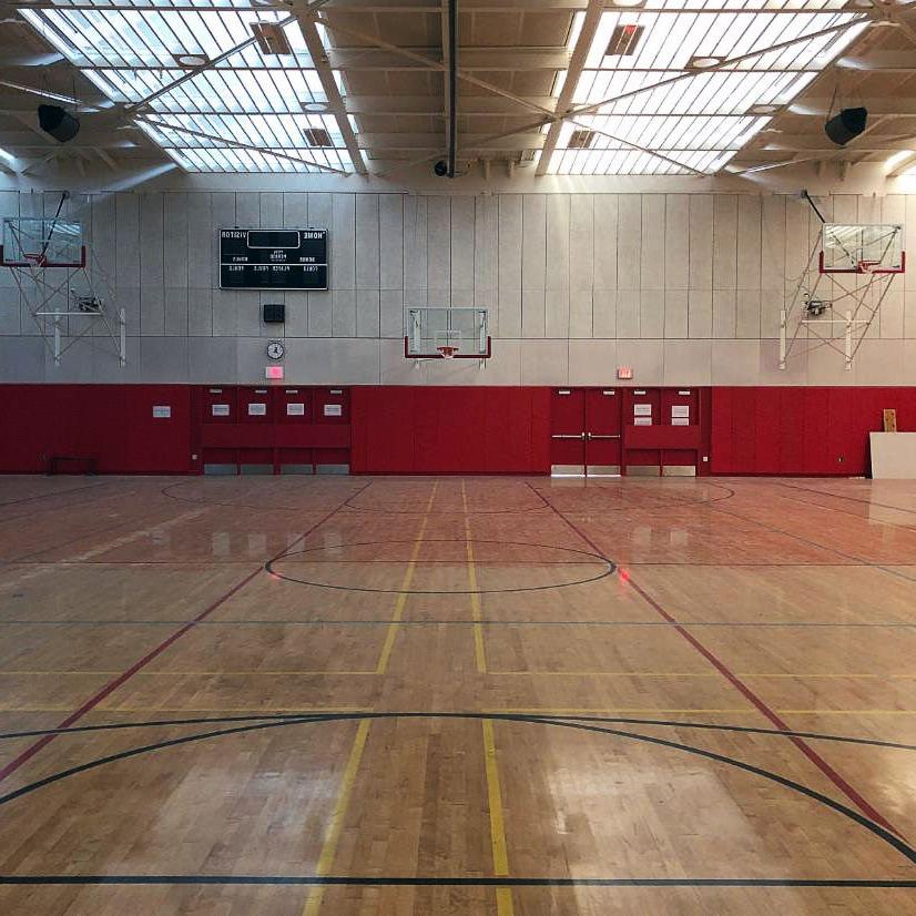 partial view of a gymnasium with a wood floor, protective padding on lower part of wall, and skylights