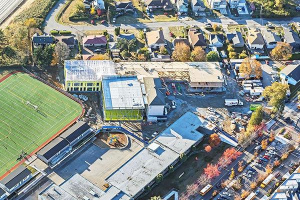 aerial view of a construction project that wraps around an existing building with a playfield to the right