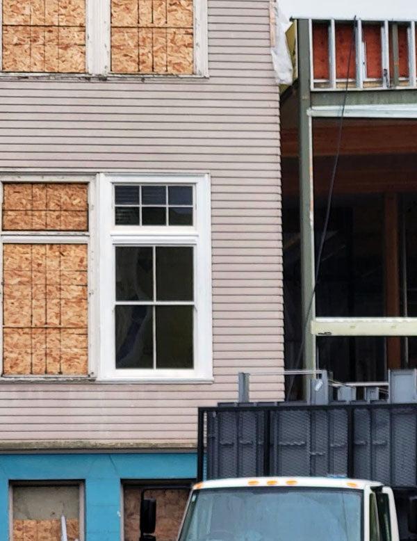 an exterior wall with one window showing and the other windows boarded up