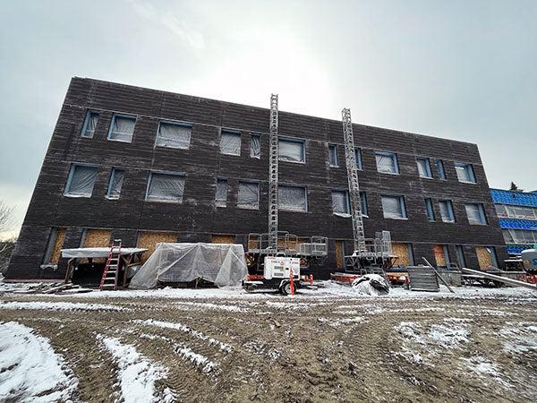 a three story brick building has boarded up window spaces on first floor and plastic covered window holes on levels 2 and 3. construction equipment is in the foreground