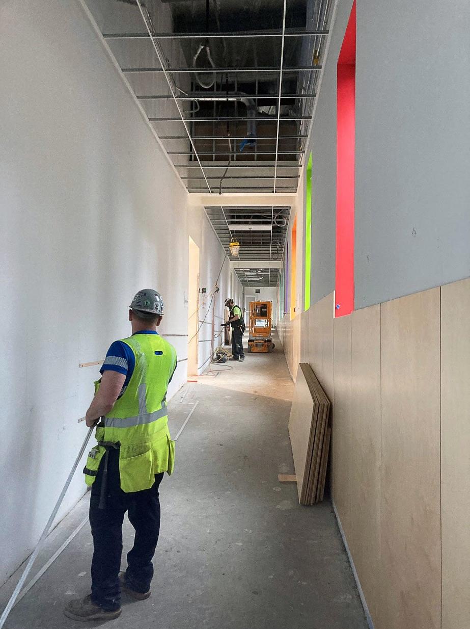 a hallway under construction has people working to install wood panels under windows with colorful window wells