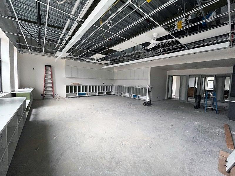 a large room with an open ceiling grid that has a fan and lights installed. casework is around the sides. on the left, doors and windows look out to an interior space