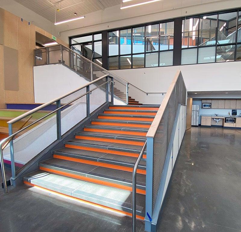 an interior stair leads up from a concrete floor past a group of windows. there is a slide next to the stairs