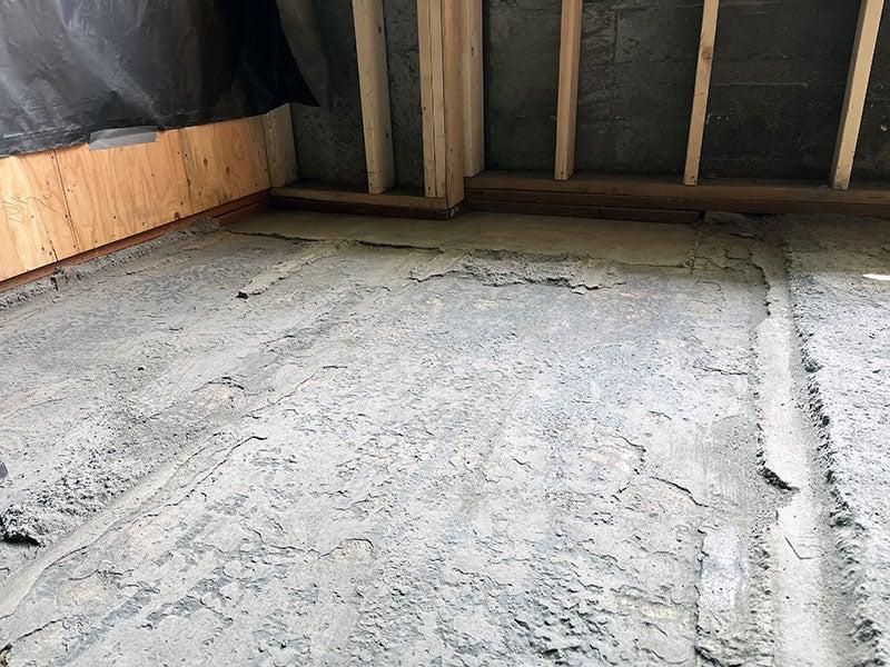 a rough concrete floor with a wall that has studs in place