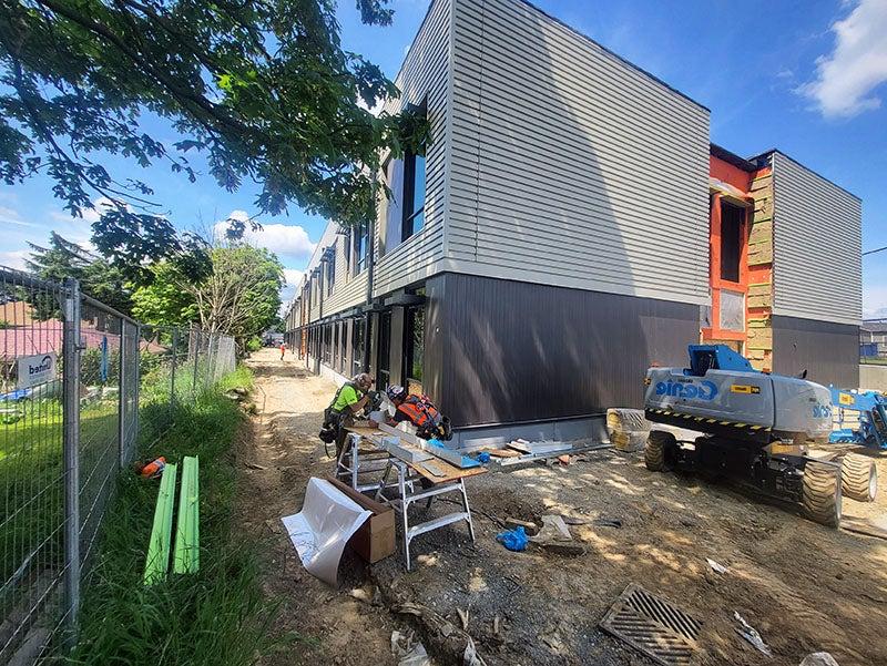 the corner of a two-story building has metal siding vertically in a dark color at the bottom and horizontally in a lighter color above