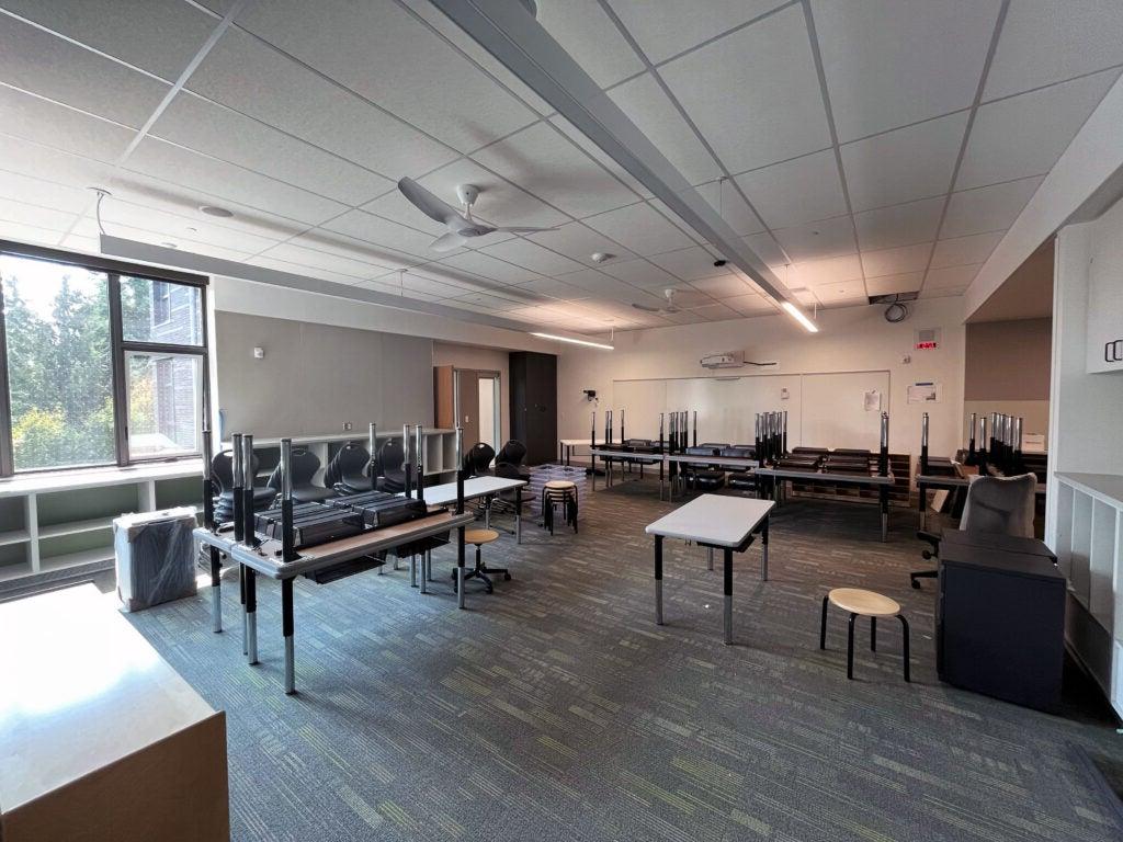 a classroom with tables and chairs stacked and a window with a bookcase below it