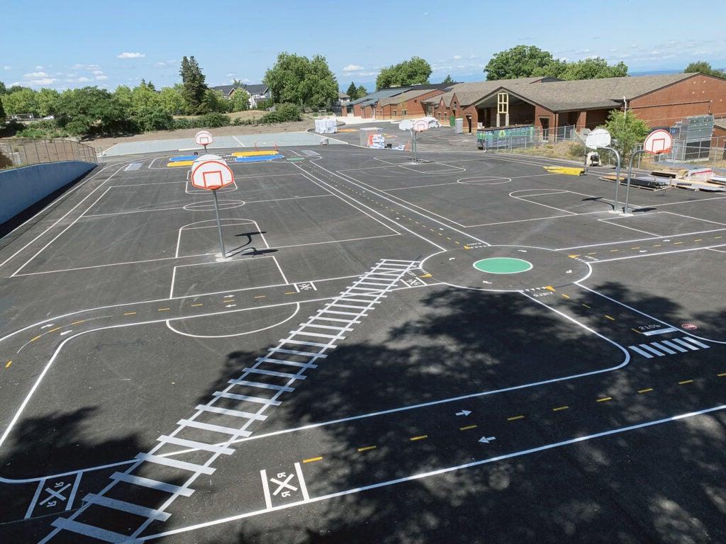 a paved area has lines for baskeball and basketball hoops, plus painted bike traffic lines