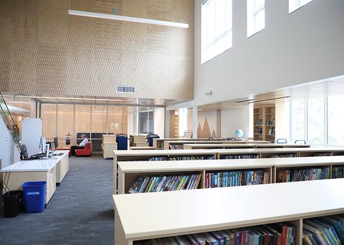 a large room has low bookshelves and a large wall of windows