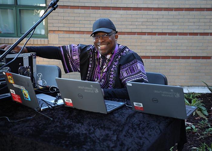 a man sits at a table with three laptops open and a microphone