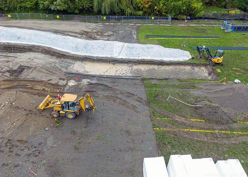 a construction site has a sloped dirt area that is next to a grass area. a back hoe and a bulldozer are in the photo