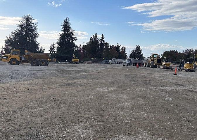 a large expanse of soil with construction vehicles. there are evergreen trees in the background.