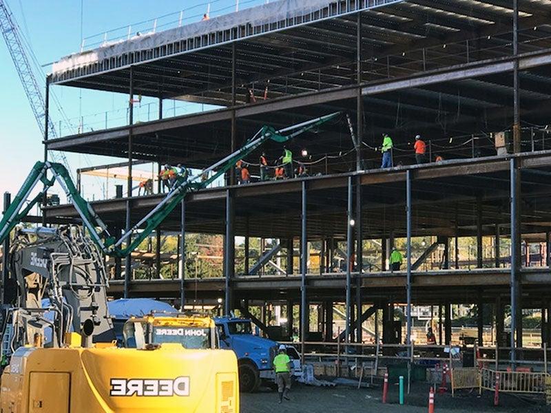 a concrete truck is pumping concrete to the third floor of a steel framed four-story building under construction