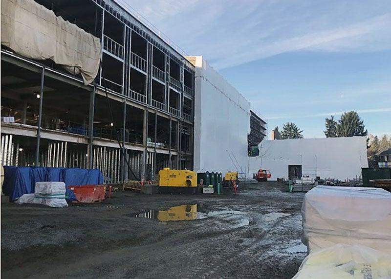 a four story frame of building has part of it wrapped in white material at a muddy construction site