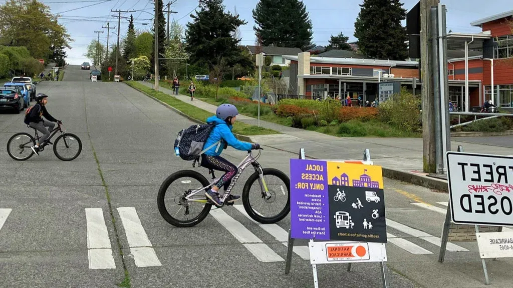 student biking on a school street closed to vehicle traffic with closure sign in foreground.