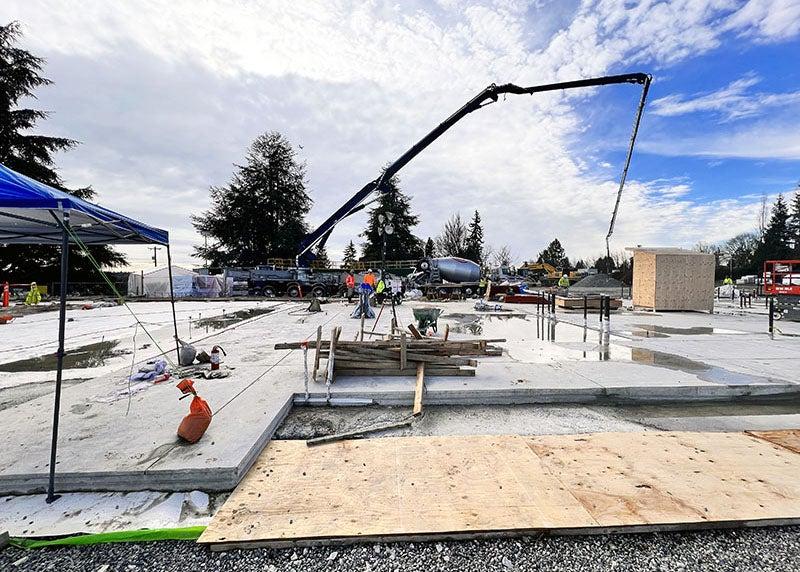 a concrete pump truck in the background with workers and a concrete slab in the foreground