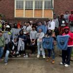 a group of young men stand in front of a brick building holding up shirts