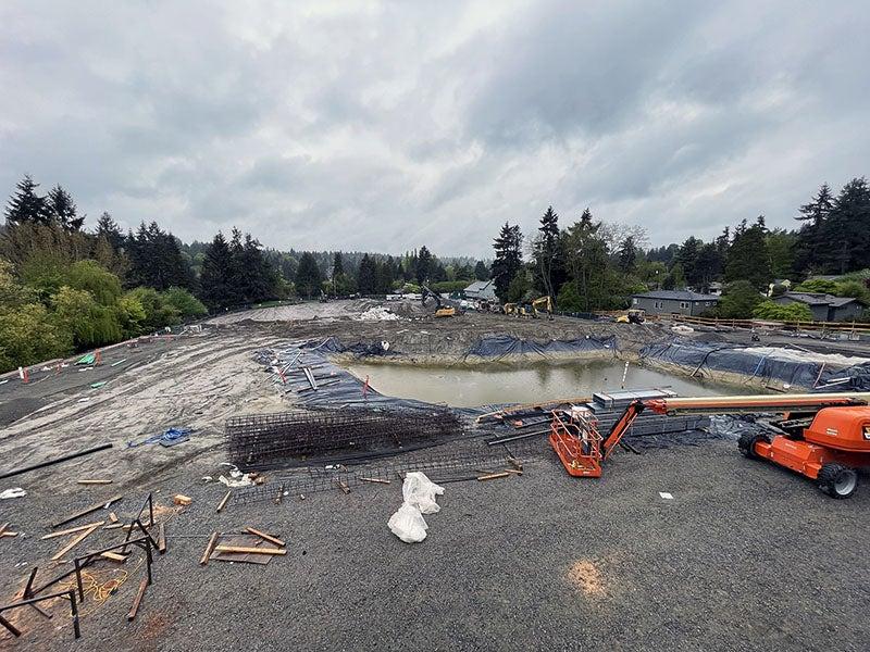 a large muddy area with a retaining pond sits behind a gravel area with a construction machine