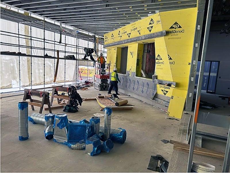 an angled yellow wall with plastic framing with workers on scaffolding