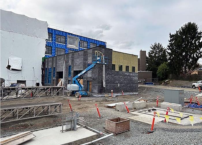 a four story building under construction with metal framing and some yellow wall covering. two lifts and workers are visible