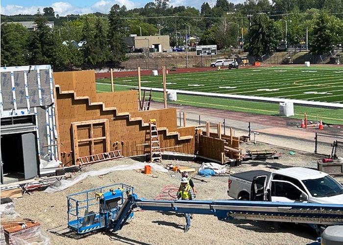 looking toward a green turf field with markings for yard lines a building under construction is in front with a tiered wall