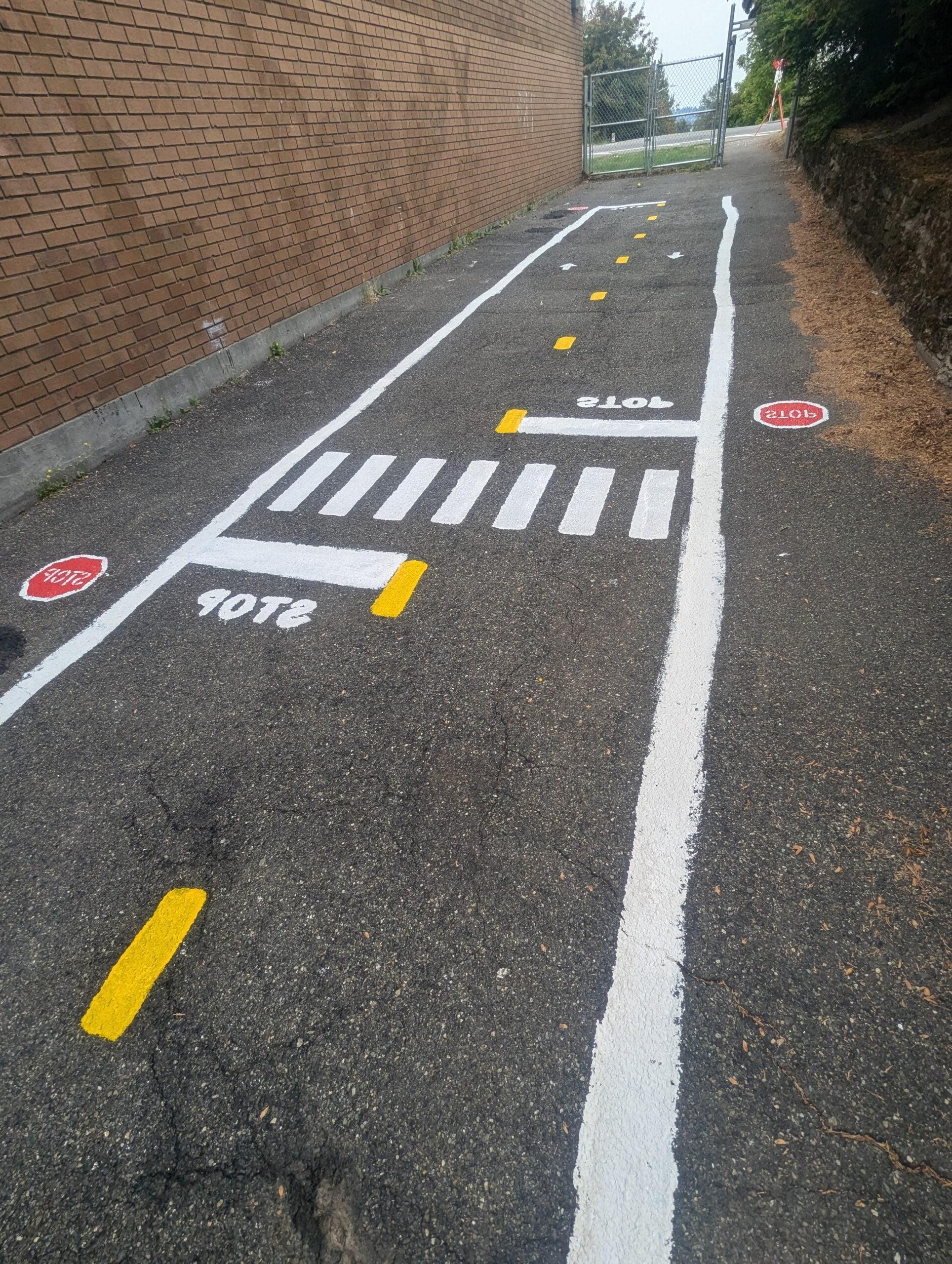 Miniature pedestrian crosswalk and stop signs on traffic garden roadway.