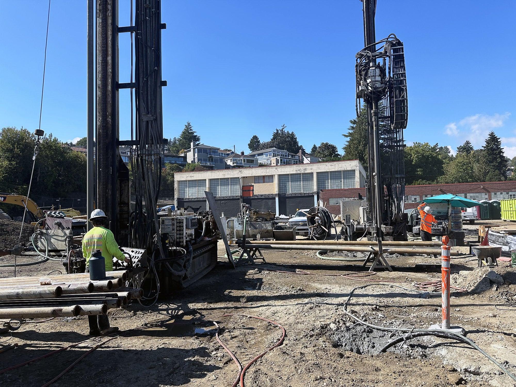 a large drilling rig with a person standing by it in a dirt field with a building behind