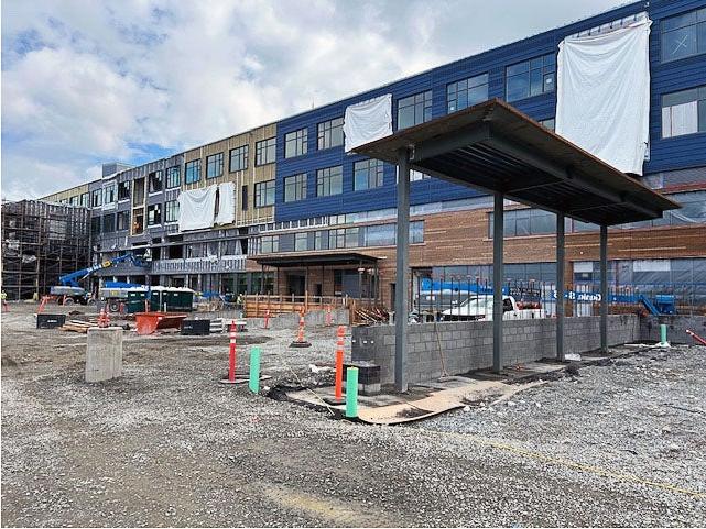 a canopy on steel posts in a gravel yard with a building under construction behind it