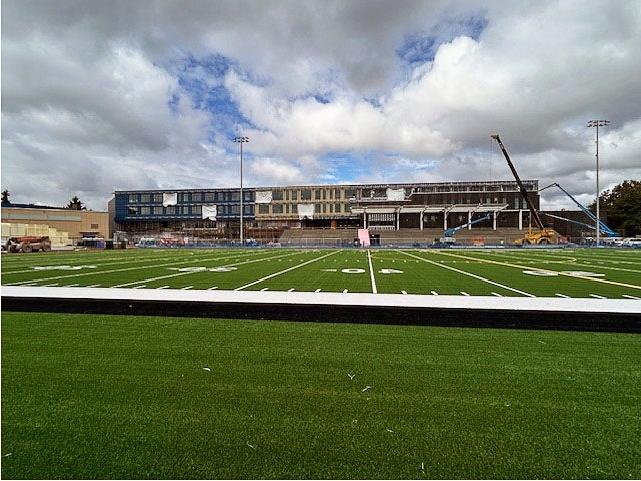 looking toward a building with construction equipment in front over a green turf field marked for football