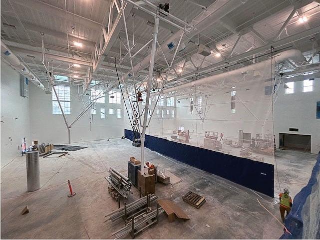 inside a very large room with zig zag rafters and construction equipment and ceiling lights