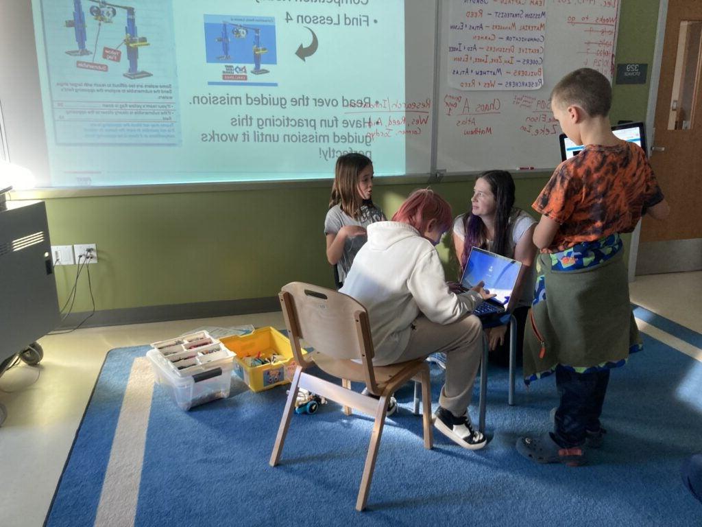 3 students gathered around teacher for robotics competition coding instruction