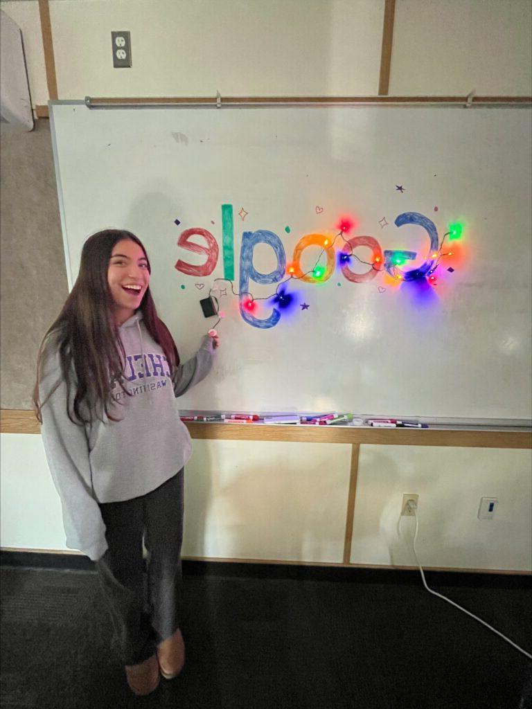 Studnet poses next to whiteboard welcoming Google volunteers