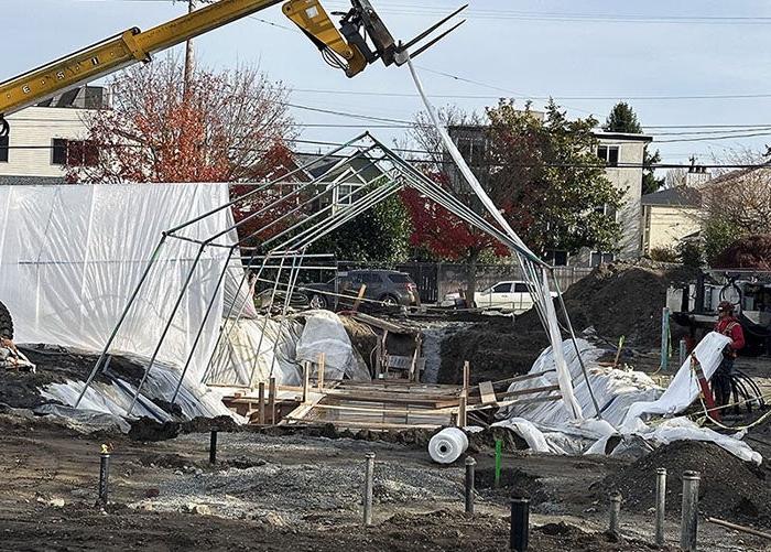 a metal tent frame with a machine lifting canvas up over it