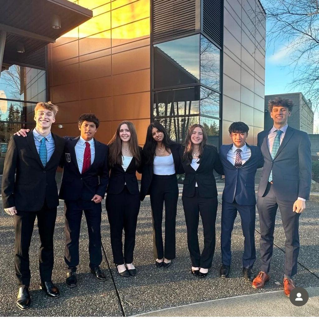 Group of students wearing suits in front of modern building