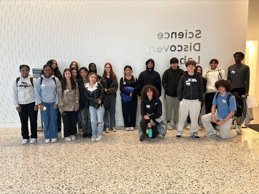 Studnets posing in front of white wall with Science Discover Lab  sign on it.