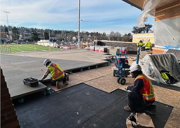 workers are laying pavers on a patio that overlooks a football field